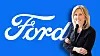 Ford executive standing with folded arms in front of a large white Ford logo on a blue background.
