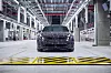 Camouflaged BMW car on an illuminated production line inside a large factory hall.