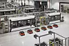 Automated factory hall with Porsche-branded battery modules on a bright production floor.