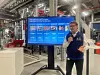 BMW employee with microphone speaking beside large screen on casting technologies in a factory.