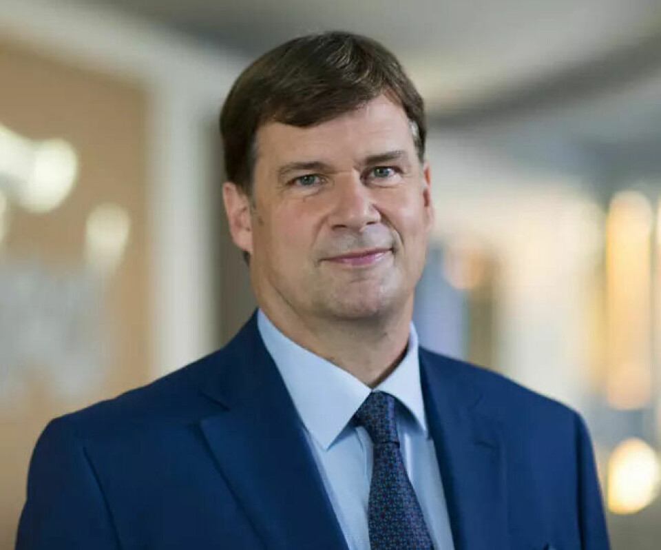 Man in a blue suit and tie standing indoors in soft focus background.