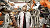 Engineer standing among orange industrial robots on a car production line.