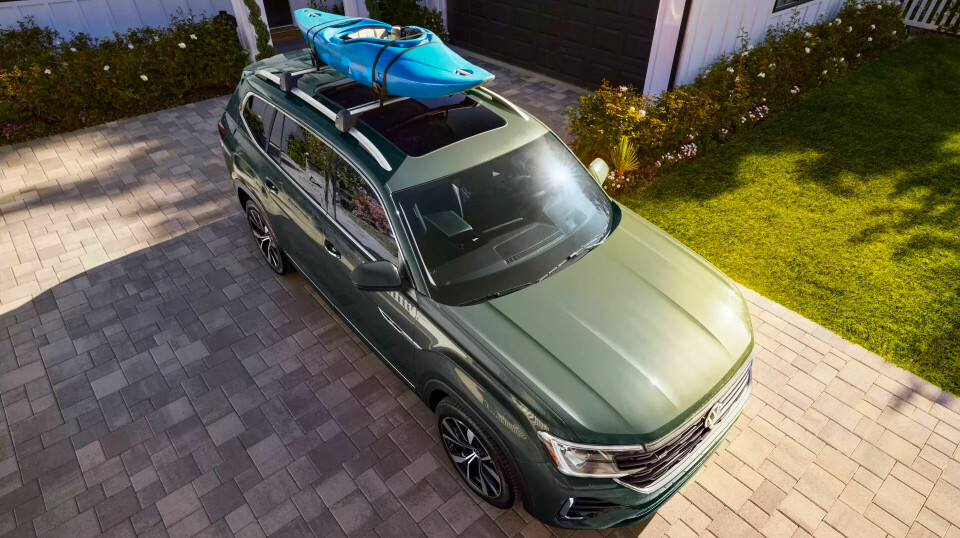 Green Volkswagen Atlas SUV with a kayak on the roof parked in a sunny driveway.