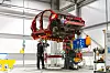 Worker dismantles a raised red car shell inside a Toyota factory workshop.