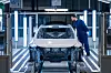 Worker examines a Volvo EX60 car body under bright lights on the Torslanda paint line.