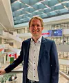 Smiling man in a dark suit stands in a bright modern office atrium.