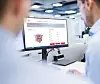 Two engineers view a Henkel LOCTITE SOLVE simulation screen on an office monitor.