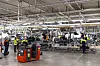 Workers assemble white SUVs on a brightly lit Volvo factory production line.