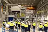 Workers in Volvo-branded high-vis jackets stand in front of a large Bühler die-casting machine inside a factory.
