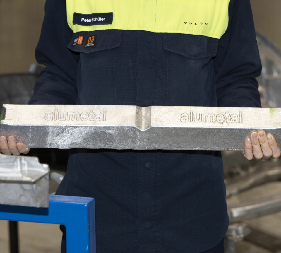 Worker in Volvo uniform holding a long aluminium casting sample in a factory.