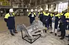 Group in safety gear examining a large aluminium car floor casting on a stand inside a factory.