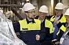 Volvo workers in helmets examine a large aluminium car floor casting inside a factory.