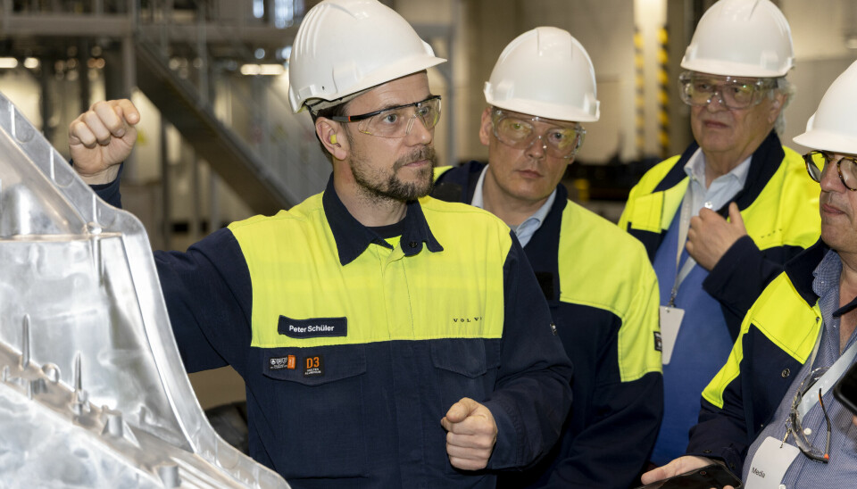 Volvo workers in helmets examine a large aluminium car floor casting inside a factory.