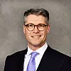Smiling man in a suit and tie posing for a formal studio portrait.