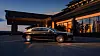 A black luxury sedan parked beside a modern building with warm interior lighting at dusk.