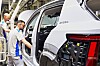 Workers assemble a white Škoda vehicle body on a factory production line.