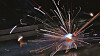 Bright welding sparks burst from a metal workpiece in a dim workshop.