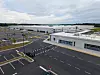 Wide view of a BMW manufacturing campus with white buildings, empty roads and parking areas beneath overcast clouds.