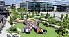 Large crowd assembled on a landscaped lawn outside a modern office and factory complex.