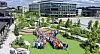 Large crowd assembled on a landscaped lawn outside a modern office and factory complex.