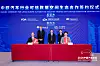 Four people stand behind a table at a blue-lit signing ceremony backdrop with company logos.