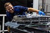 A worker in blue safety clothing inspects battery assembly machinery in an industrial plant.