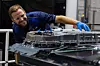 A worker in blue safety clothing inspects battery assembly machinery in an industrial plant.
