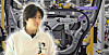 A person stands in front of an industrial assembly line with metal machinery, cables and purple signage.
