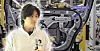 A person stands in front of an industrial assembly line with metal machinery, cables and purple signage.