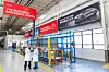 Two people in lab coats stand in a bright industrial facility with Henkel and Bonderite signage and testing equipment.
