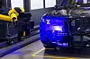 A yellow robotic arm beside the front end of a dark BMW SUV in a factory setting.
