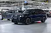 A dark BMW X5 SUV on an assembly line inside a bright automotive factory.