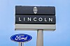 Lincoln and Ford roadside signs mounted on tall poles against a blue sky.