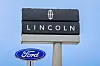 Lincoln and Ford roadside signs mounted on tall poles against a blue sky.