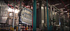 Large metal vehicle body panels hang in an industrial plant beside pretreatment equipment and piping.