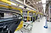 Automated factory line with car bodies, yellow rails, and industrial machinery inside a large production hall.