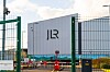A JLR building behind green security gates and barriers at an industrial site.