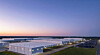 Aerial view of a battery storage site with white warehouse buildings and containers under a dusk sky.