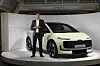 Ein Mann steht neben einem hellen Audi A2 e-tron auf einer Messebühne.
