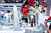 Red robotic arm working inside a car factory beside a vehicle body frame.