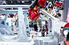 Red robotic arm working inside a car factory beside a vehicle body frame.