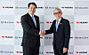 Two suited men shake hands in front of Mazda and Yazaki logo backdrops.