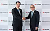 Two suited men shake hands in front of Mazda and Yazaki logo backdrops.