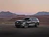 A grey Audi SUV parked on a road with desert mesas and hills in the background at sunset.