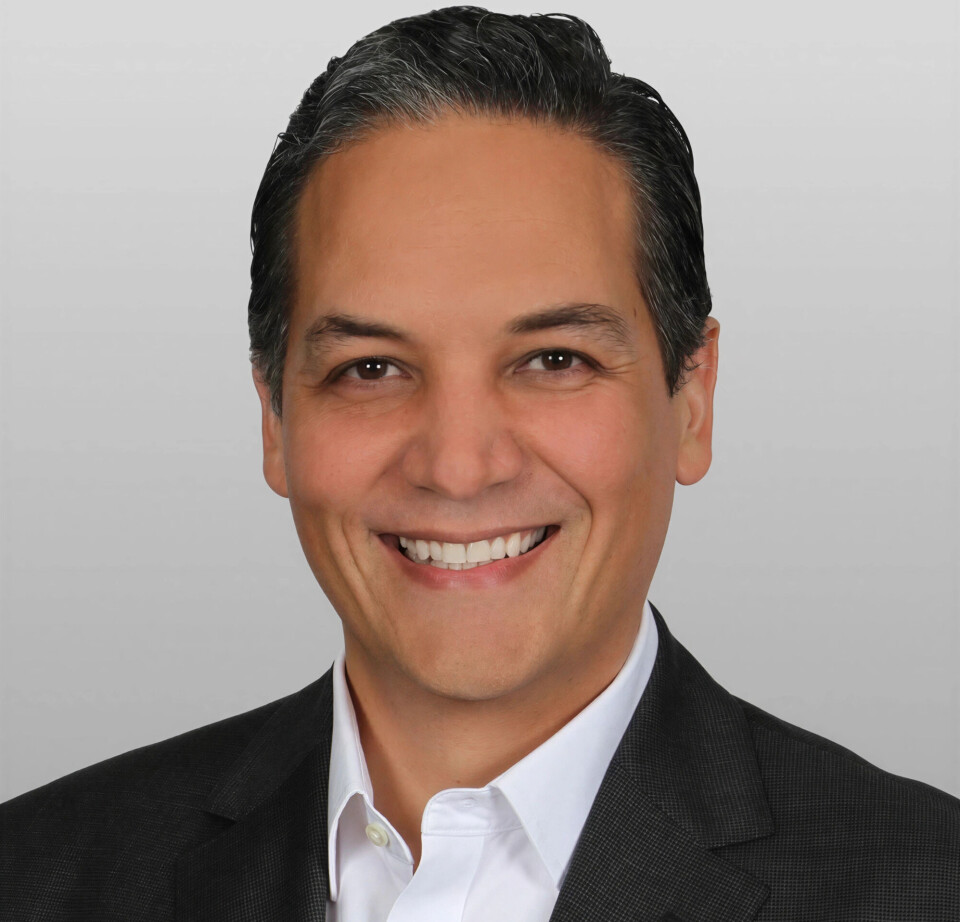 Studio portrait of a smiling man in a dark suit and white shirt on a grey background.